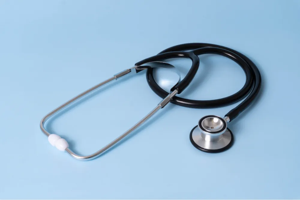 A black stethoscope with silver accents lies on a light blue background.