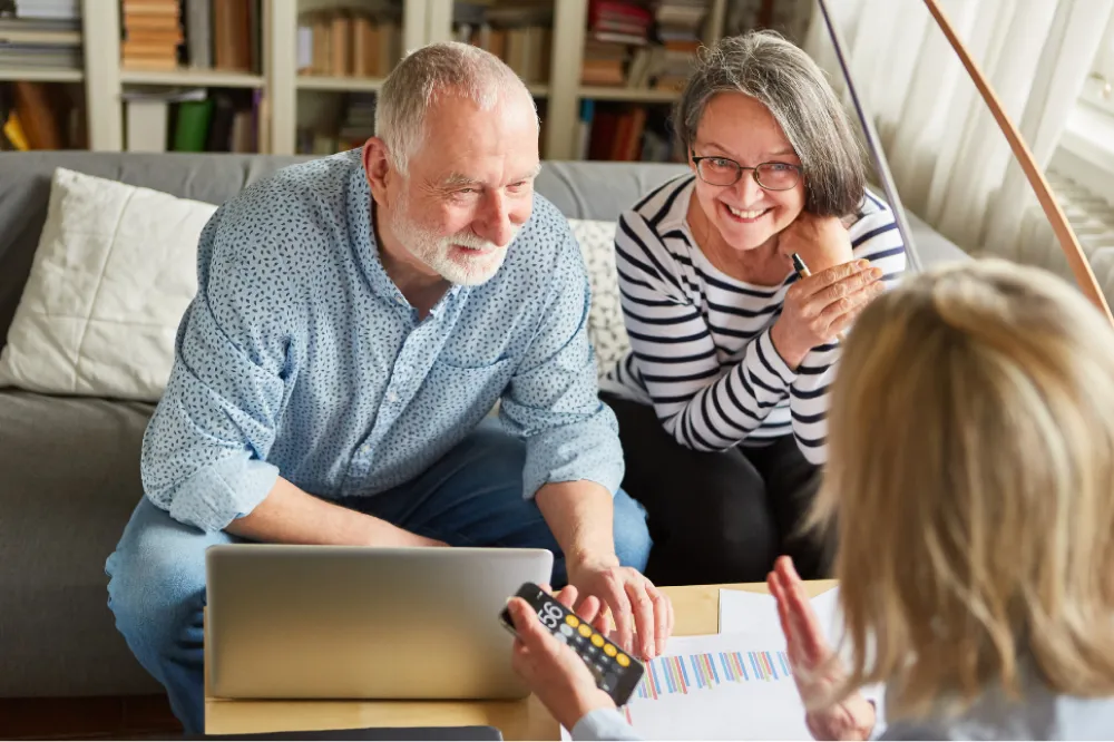 Smiling older couple sitting by a laptop, discussing finances with a person holding a calculator.